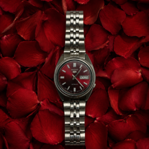 Seiko automatic men's stainless steel watch with a red dial displayed on red rose petals.